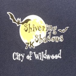 Logo featuring a yellow moon with bat silhouettes and the text 'Shivering Shadows 7K' above 'City of Wildwood' in gothic font.