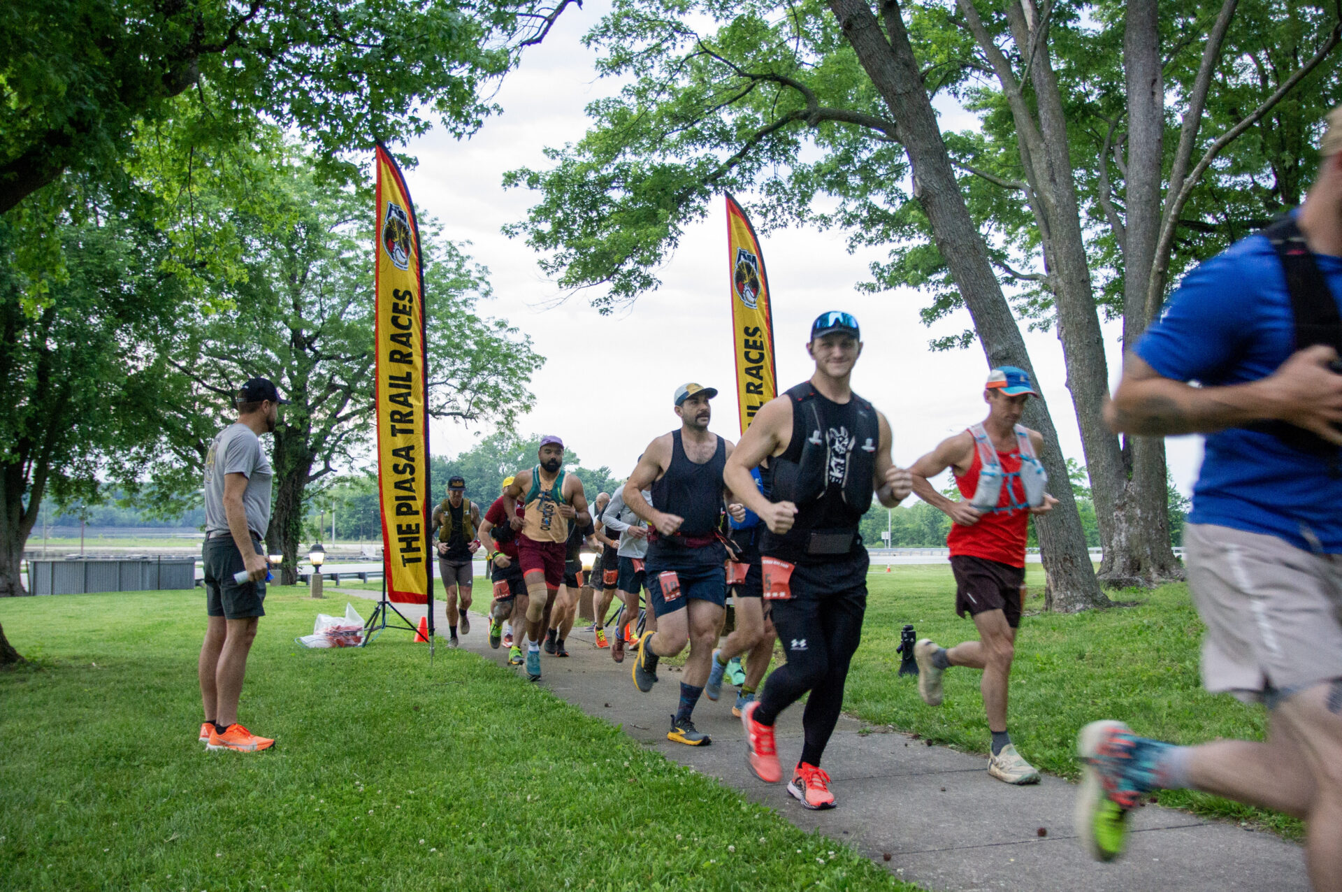 Group of runners on a park path during a race, with yellow banners and trees overhead.